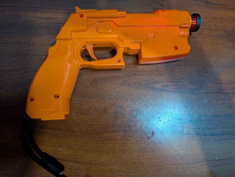 Namco GunCon 2 controller, with a fisheye lens over the muzzle and two cables coming from the bottom of the grip.
