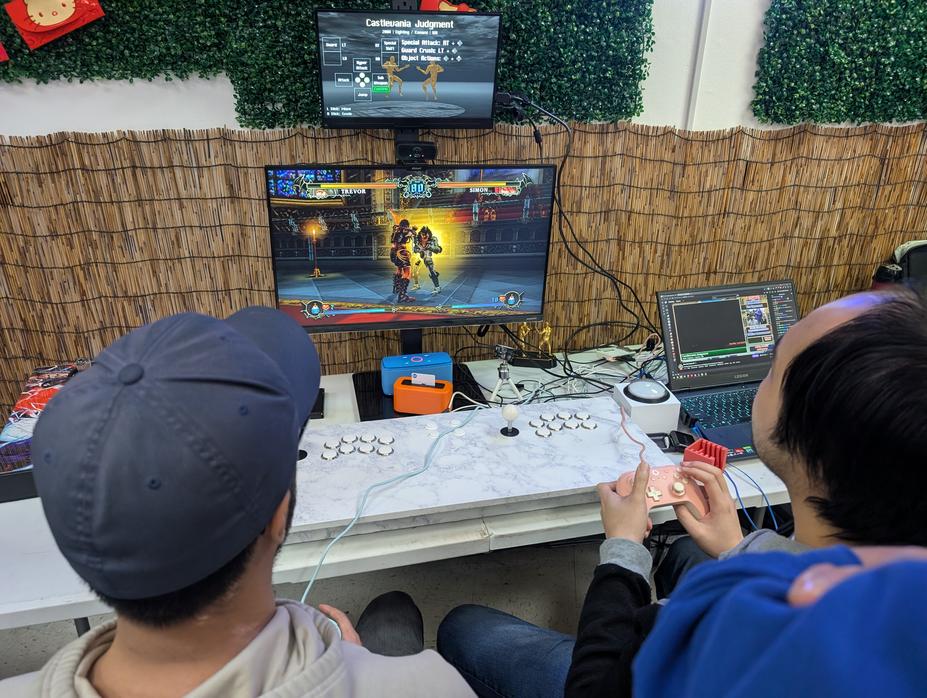 Tournament station showing Castlevania Judgment for the Nintendo Wii. The players use standard game pads rather than the arcade controls for this game.